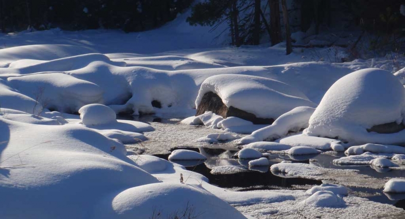 A mostly frozen creek winds through a snowy landscape